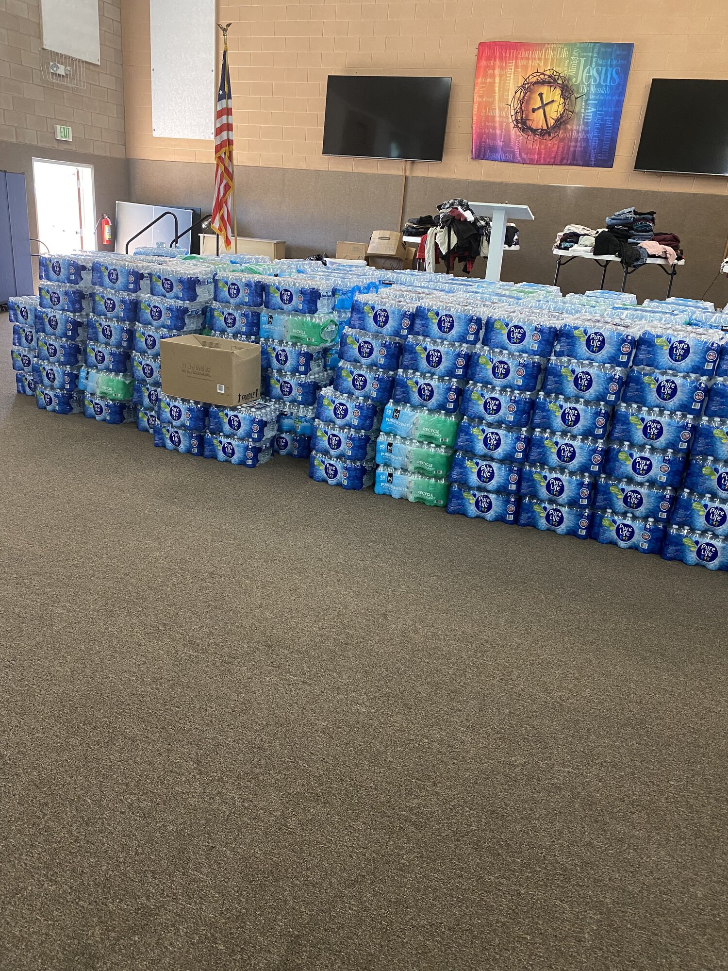 Rows of donated bottled water filling the church hall beside an American flag