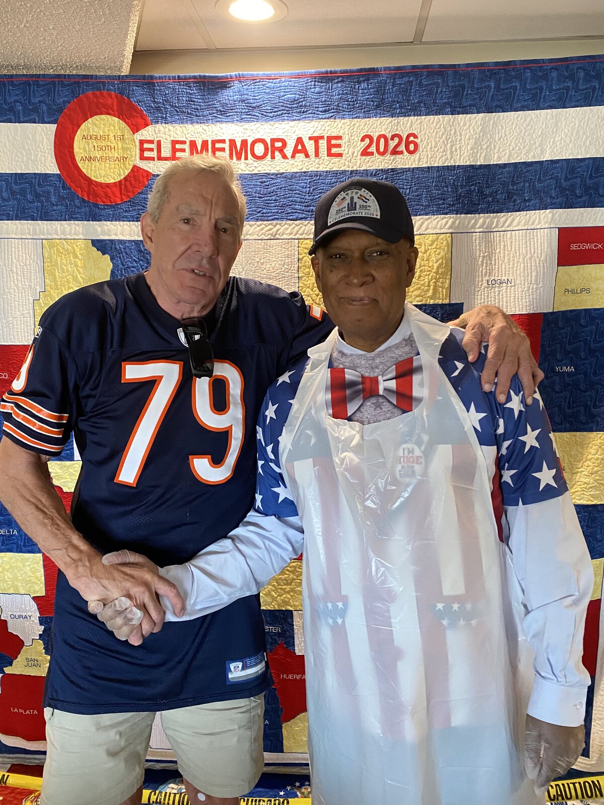 Big Tony shaking hands with John Hoffman in front of the Celememorate 2026 quilt