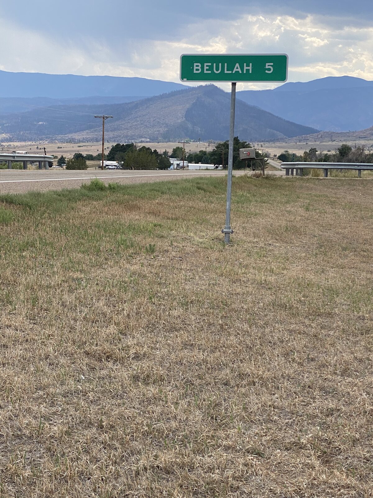 The Beulah highway sign with the fire-scarred mountainside visible in the distance behind it